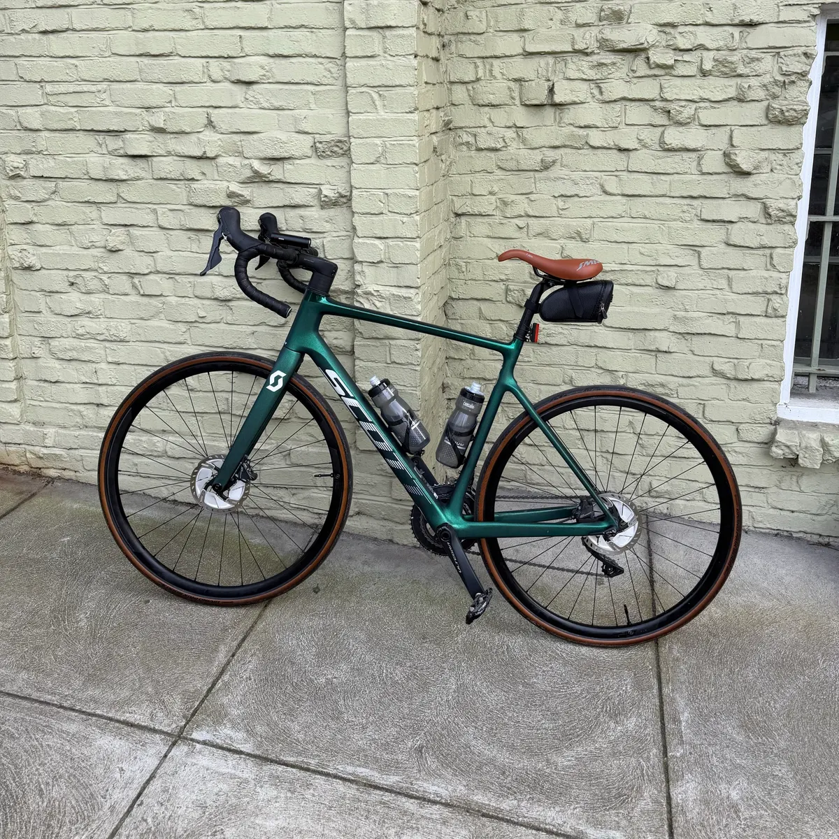 A green road bike leaning against a pale painted brick wall