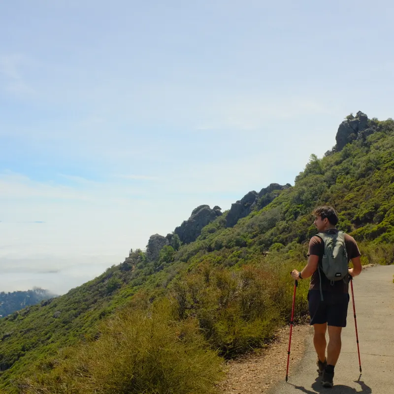 A hiker with trekking poles on a trail toward rocky peaks
